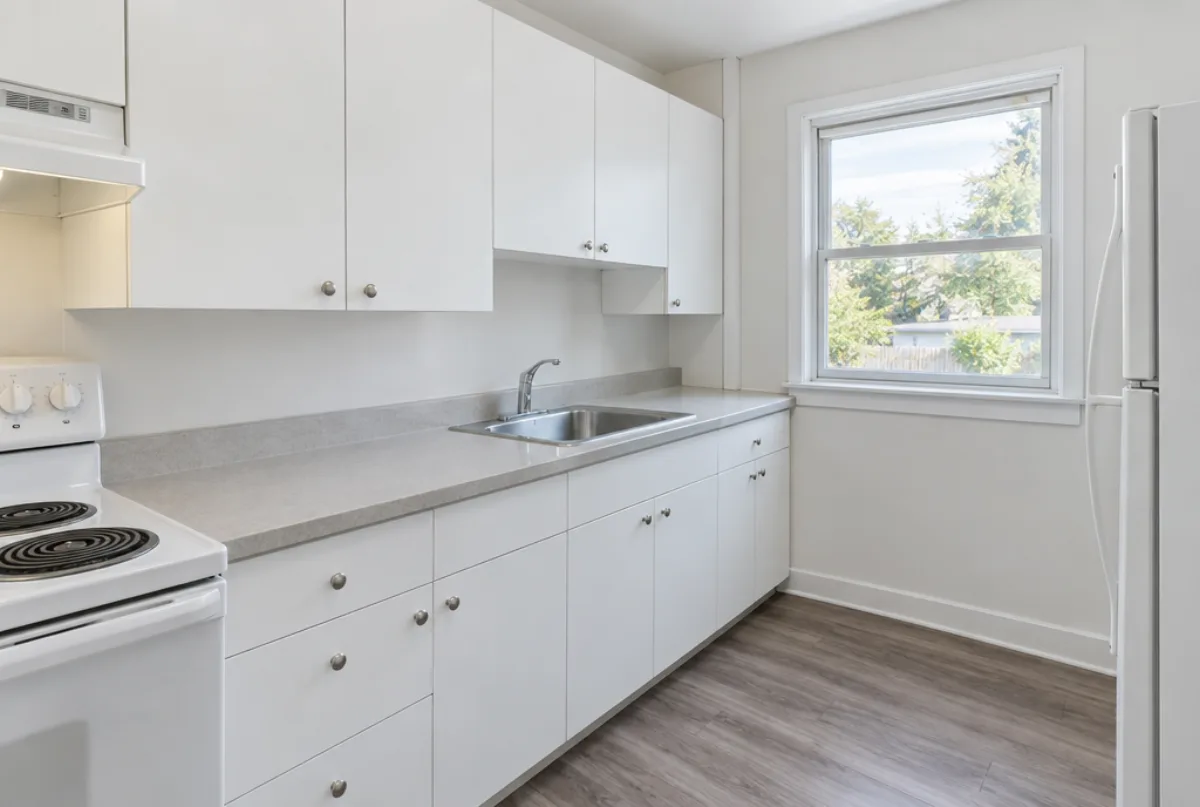 Simple bright kitchen with white flat-panel stock cabinets, a laminate counter, a white range and refrigerator and a window over the sink